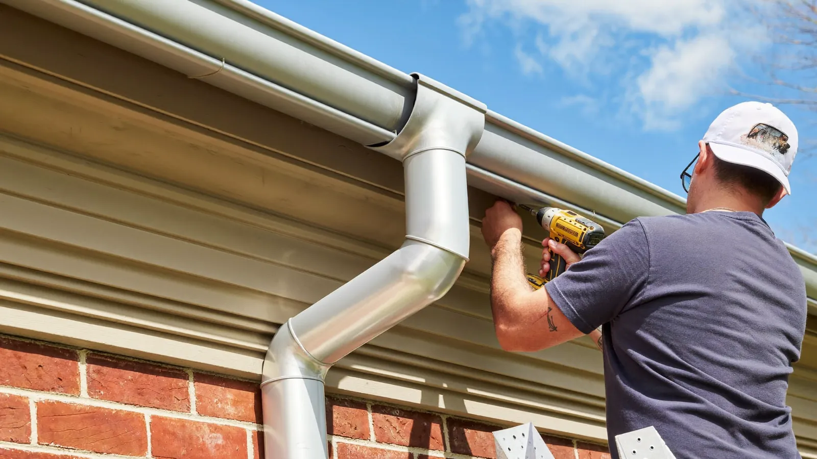 Installer fitting a length of seamless aluminum gutter to the fascia board along the eave of a brick home in Tennessee